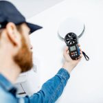 Handyman checking the speed of air ventilation with measuring tool on the white wall background